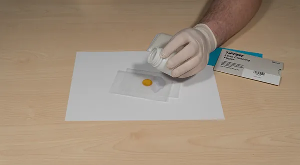 Applying a few drops of alcohol to lens cleaning paper laid over the lens