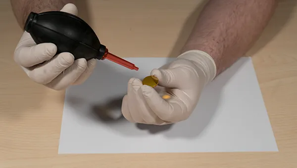 Blowing loose dust off the lens with an air blower held at an angle
